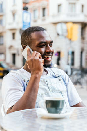 Attractive african man taking by phone on a bar terraceの写真素材