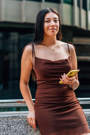 chinese young woman holding a yellow phone in the street and smiling to cameraの写真素材