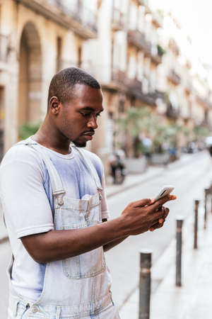 vertical portrait of an african american young man waiting in the street ans using his phoneの写真素材