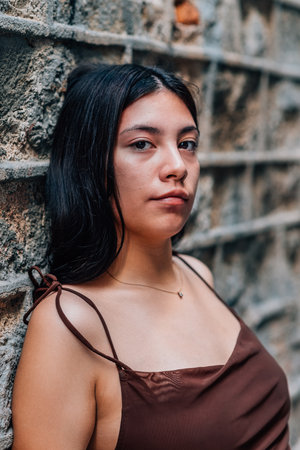 vertical portrait of an attractive and young asian woman leaning on a wall and looking at cameraの写真素材