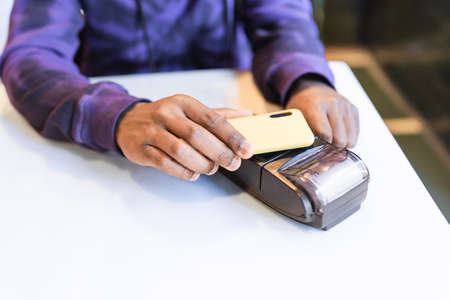 Black guy using smartphone for online payment through terminalの写真素材