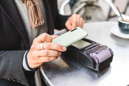 Crop cafe customer paying for order via cellphone