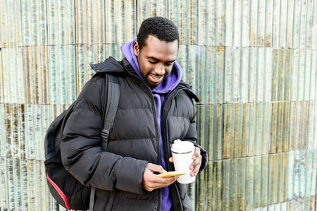Black man with coffee to go using smartphone
