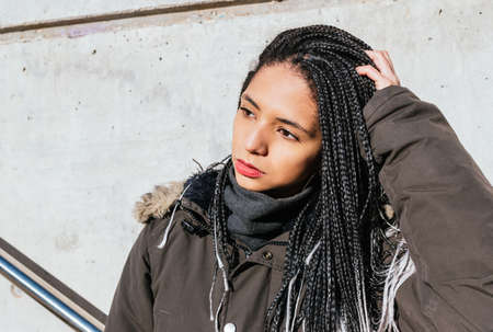 Stylish woman touching braided hair in city