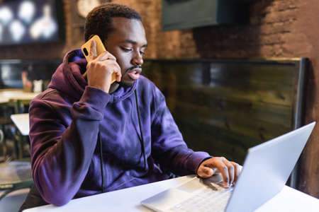 Serious black man speaking on cellphone and typing on laptop