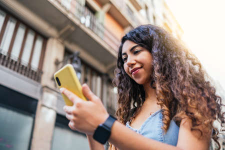 Attractive young woman using phone while walking the streets in summerの写真素材