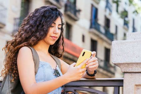 turkish woman with a backpack checking her smartphone in the streetの写真素材