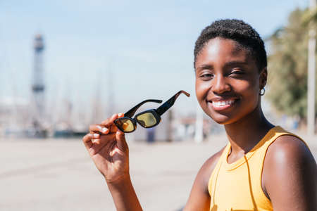 attractive african woman looking at camera and holding sunglasses