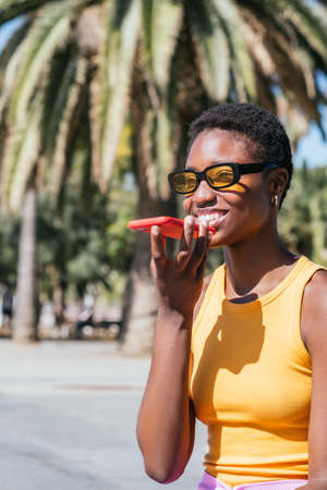 stylish african woman sending voice message outdoors on a sunny dayの写真素材