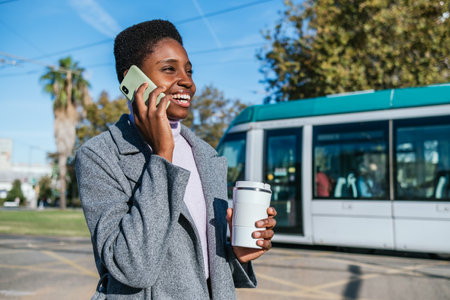 Glad African American female answering phone call near tram