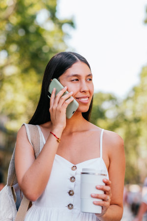 Hispanic woman with hot drink having smartphone conversationの写真素材