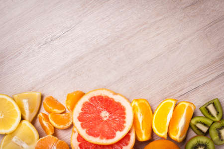 lemon, orange, kiwi, grapefruit, mandarin on a wooden surface. arrangement of sliced fruit. Top view with copy space for text.の写真素材