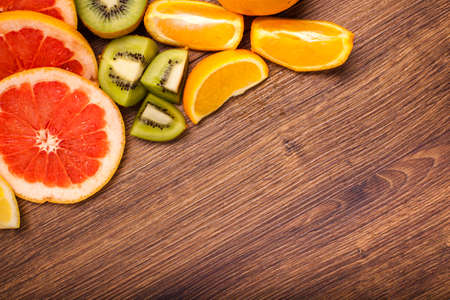 lemon, orange, kiwi, grapefruit, mandarin on a wooden surface. arrangement of sliced fruit. Top view with copy space for text.の写真素材