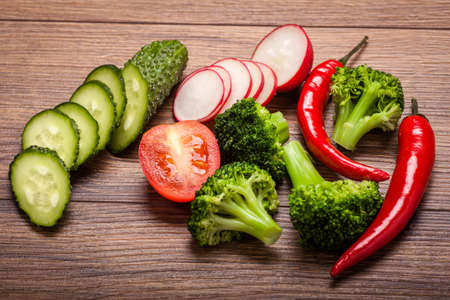 tomato, radish, cucumber and broccoli, chili on a wooden surface. arrangement of sliced vegetables.