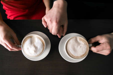 young couple sitting and drinking coffee at cafe restaurant. two cups with coffee are on table. hands of man and woman. people in loveの写真素材