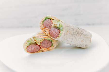 Shawarma sandwich - fresh roll of thin lavash (pita bread) filled with grilled meat, mushrooms, cheese, cabbage, carrots, sauce, green. Traditional Eastern snack. On a wooden background.の写真素材