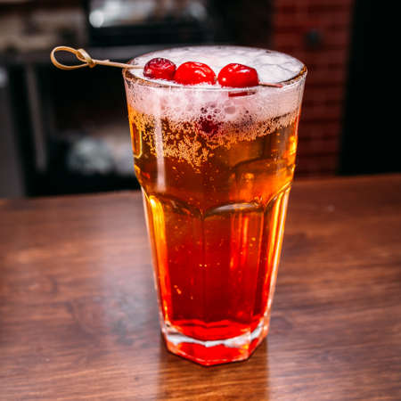 a glass of beautiful bright cocktail on a wooden surface decorated with fruits, berries, leaf of mint and basil at bar counter background.の写真素材