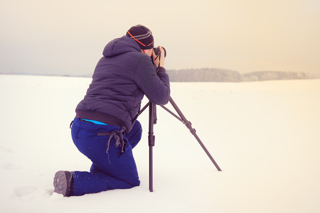 A traveler on the background of winter landscape.Young photographer smitrit forward on the banks of...
