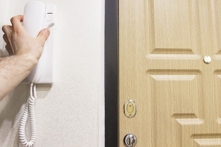 The man's hand takes the phone's doorphone against the door in the house. Answer the intercom when...