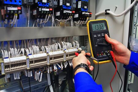 engineer tests the industrial electrical circuits with a multimeter in the control terminal box....