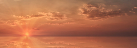 Panoramic view of the evening colorful sky with clouds at sunset leaving for the horizon. Bright sun rays in a red sky with clouds at sunset.の写真素材