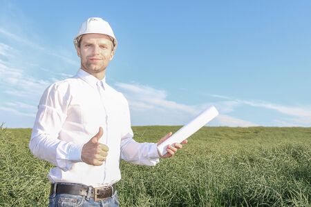 Happy engineer architect in white helmet with blueprints holding his thumb up and smiling. A...