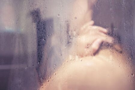 Young girl in shower behind glass with dropsの写真素材