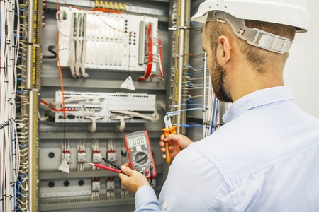 Electrical engineer adjusts control cabinet with multimeter and wire cutters. Testing of electrical...