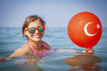 happy girl bathes in sea water. Vacation in Turkey. Turkish flag on balloon. Smiling girl on seaの写真素材