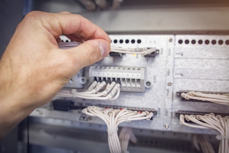 engineer connects wires to the connector of industrial control controller in electrical cabinet closeupの写真素材