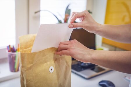 Woman inserts document into brown envelope on the background of office close-up. Female hands and brown envelopeの写真素材