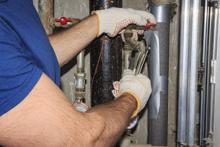 plumber repairs pipes in plumbing unit. Tools plumbing in hand against background of pressure...