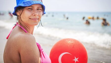 Young beautiful woman holds balloon with turkish flag on it on tropical beach on summer sunny day. Resort in Turkey. Vacation on sea beachの写真素材
