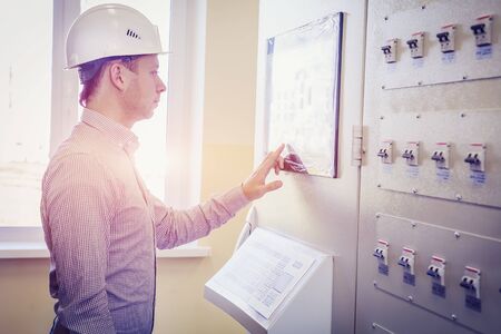 engineer controls technological process on control panel. Serviceman in white helmet monitors the...