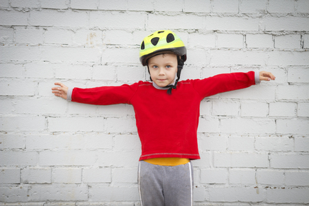 Portrait of caucasian boy in helmet with arms outstretched against white wall background.の写真素材
