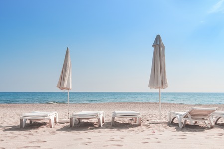 Summer rest on sea beach background. Deckchair or sunbeds with umbrellas on white sand of resort beach on sunny clear day. Beach, sea and sky on horizon. Resort vacation on sandy sea beachの写真素材