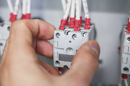 hand of electrician installs package switch with connected wires in electric control panel close up