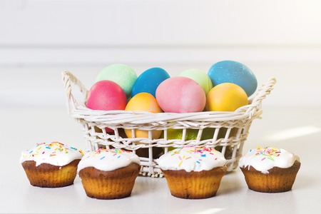 Holiday Easter concept. Multicolored easter eggs in a basket, sweet cupcakes. Easter background....