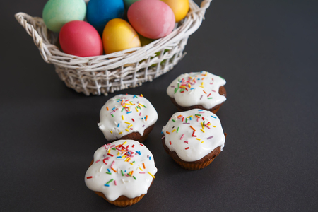 Colorful Easter eggs in basket and sweet muffins cupcakes on a black background. Easter background....