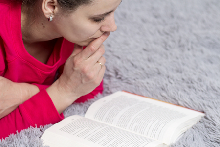 A young girl is reading a book close-up. A woman lies on a bed and carefully reads a book at home. Hobby to read books concept.の写真素材