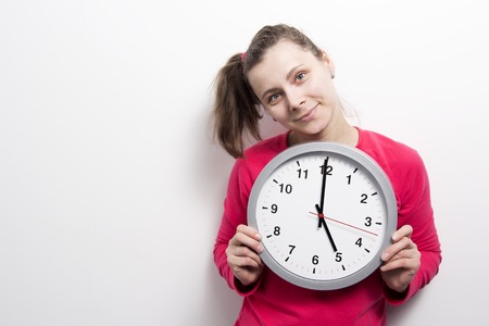 girl is holding round clock on white background. Time concept. Young woman with clock in hands. Portrait of smiling girl with wall clock. Keep, manage and stop timeの写真素材
