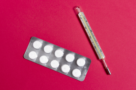 Pills and thermometer on pink background close-up. Treat the disease concept. The man in the...