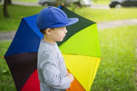 Little boy in hat with multicolor umbrella in park after rain on sunny summer day.の写真素材