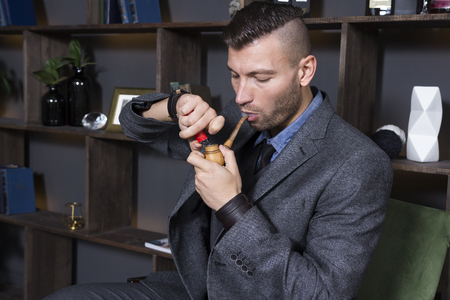 Elegant handsome man in a suit smokes a pipe in his officeの写真素材
