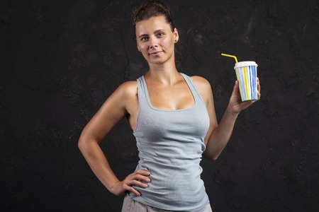 Studio portrait of fitness girl with milkshake on black background. Sport woman in gym. Attractive...