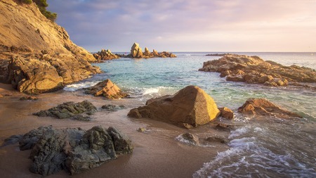 Scenery beach at sunrise. Spanish beach. Rocks and stones on sea shore. Amazing view on sea. Spanish tropical beach at dawn in warm sunlight.の写真素材