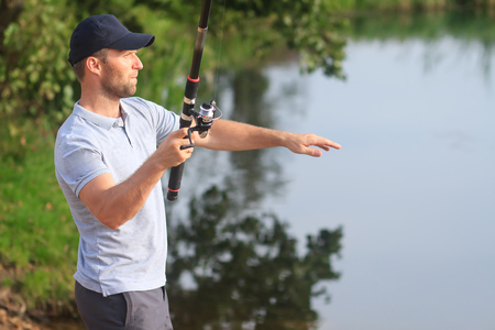 Fisherman with fishing rod on river bank. Fisher catching fish in lake