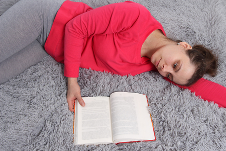 Dreaming woman with book on bed. girl thinks about book readの写真素材