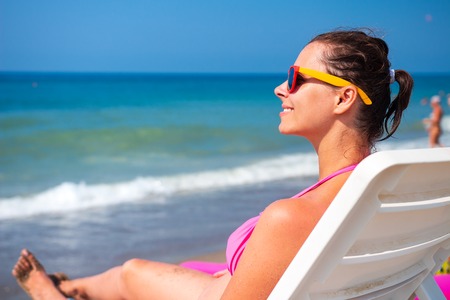 Summer vacation on seaside. Woman relaxes on deckchair against blue sea water. Girl sunbathing on...