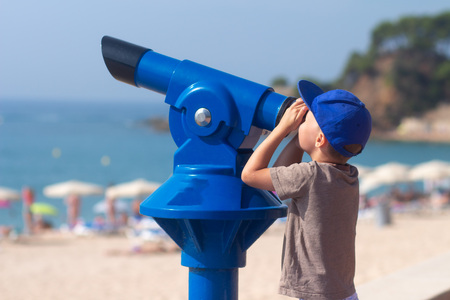 Happy little boy looking in telescope at Lloret beach. Lloret de Mar, Costa Brava, Spainの写真素材